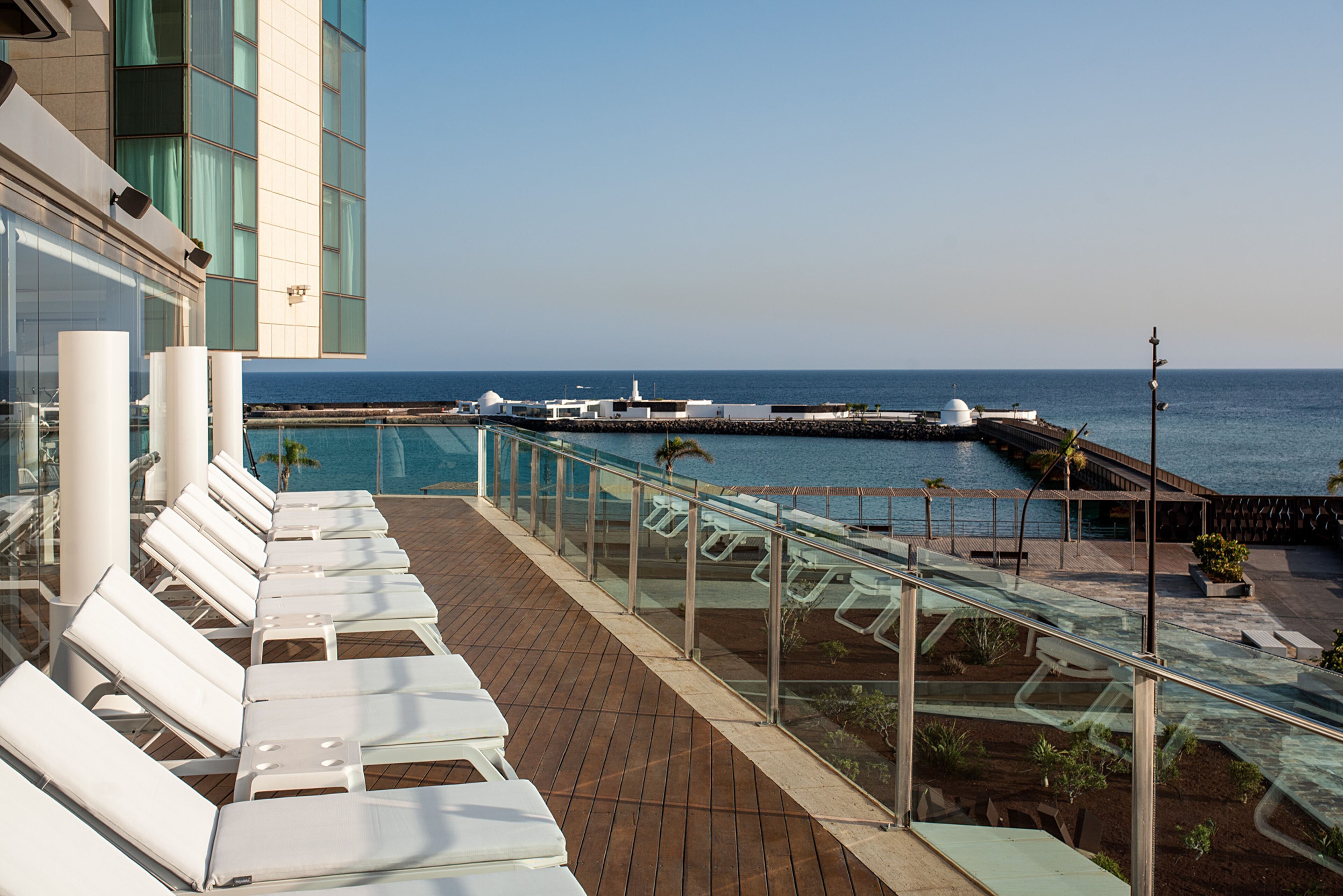 A deck with sun loungers overlooking the sea, a glass railing, and a view of the ocean.