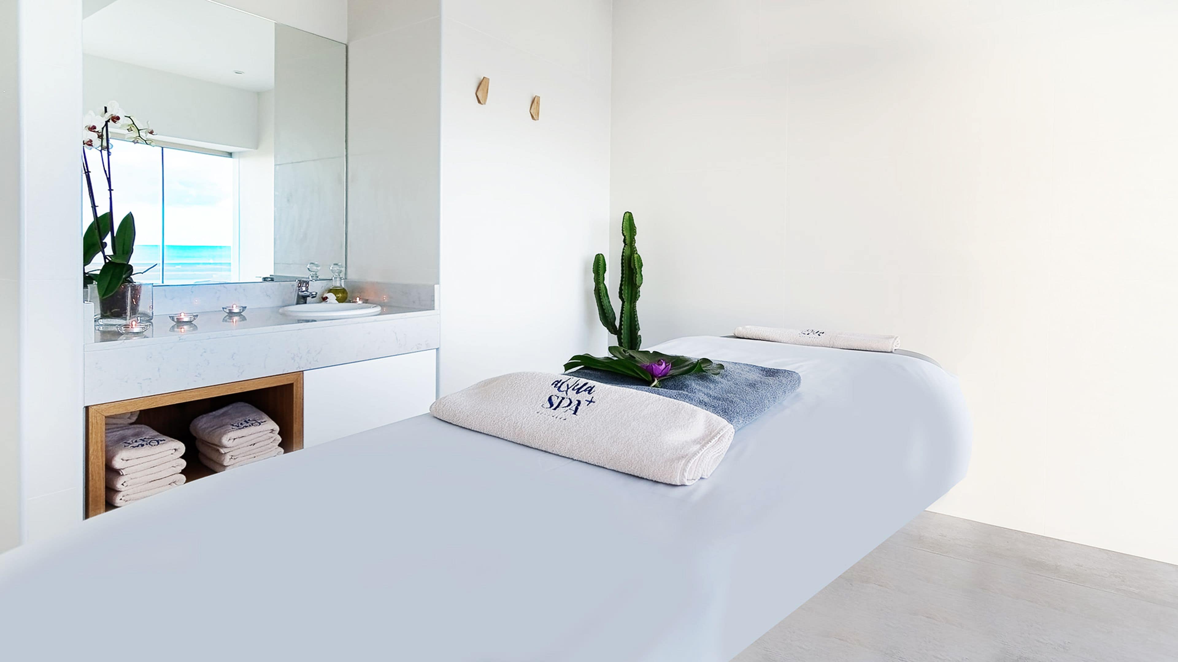 A modern spa room with a large mirror, a sink, and a massage table.