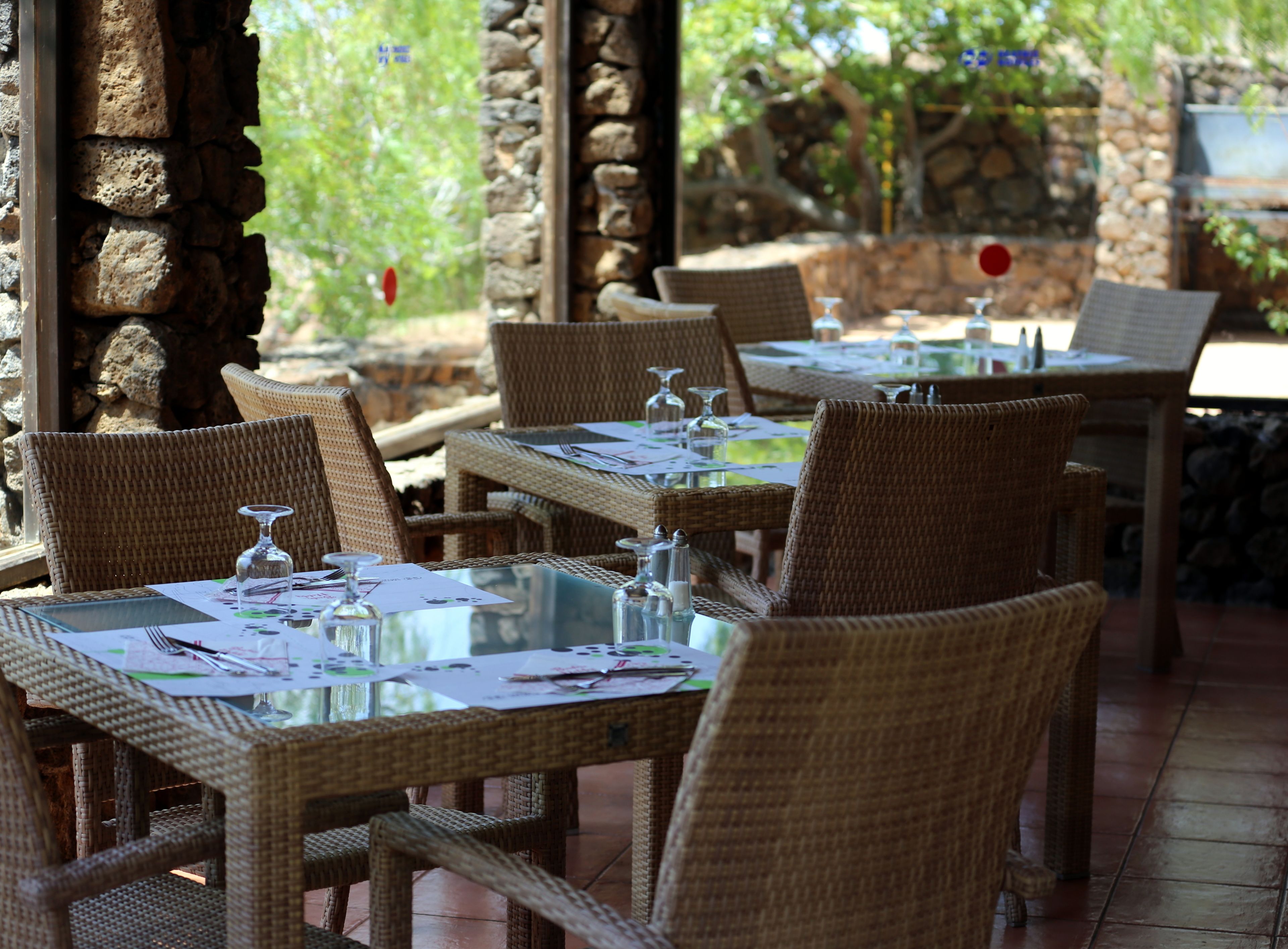Ein Restaurant mit Korbtischen und -stühlen, Steinwänden und Blick ins Grüne.