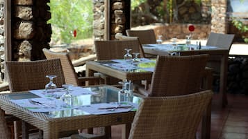 Un restaurante con mesas y sillas de mimbre, paredes de piedra y vistas a zonas verdes.
