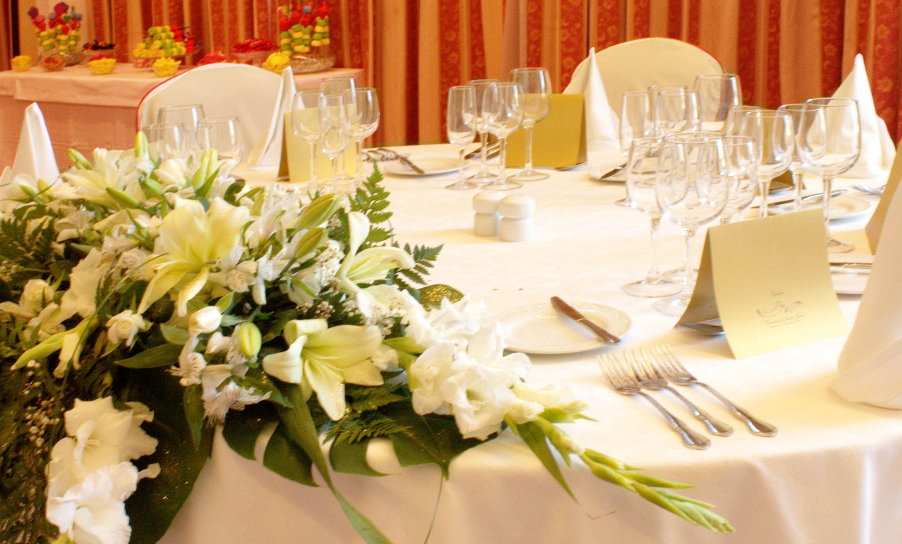 Una mesa dispuesta para un evento formal, con un centro de mesa floral, mantel blanco y cristalería.