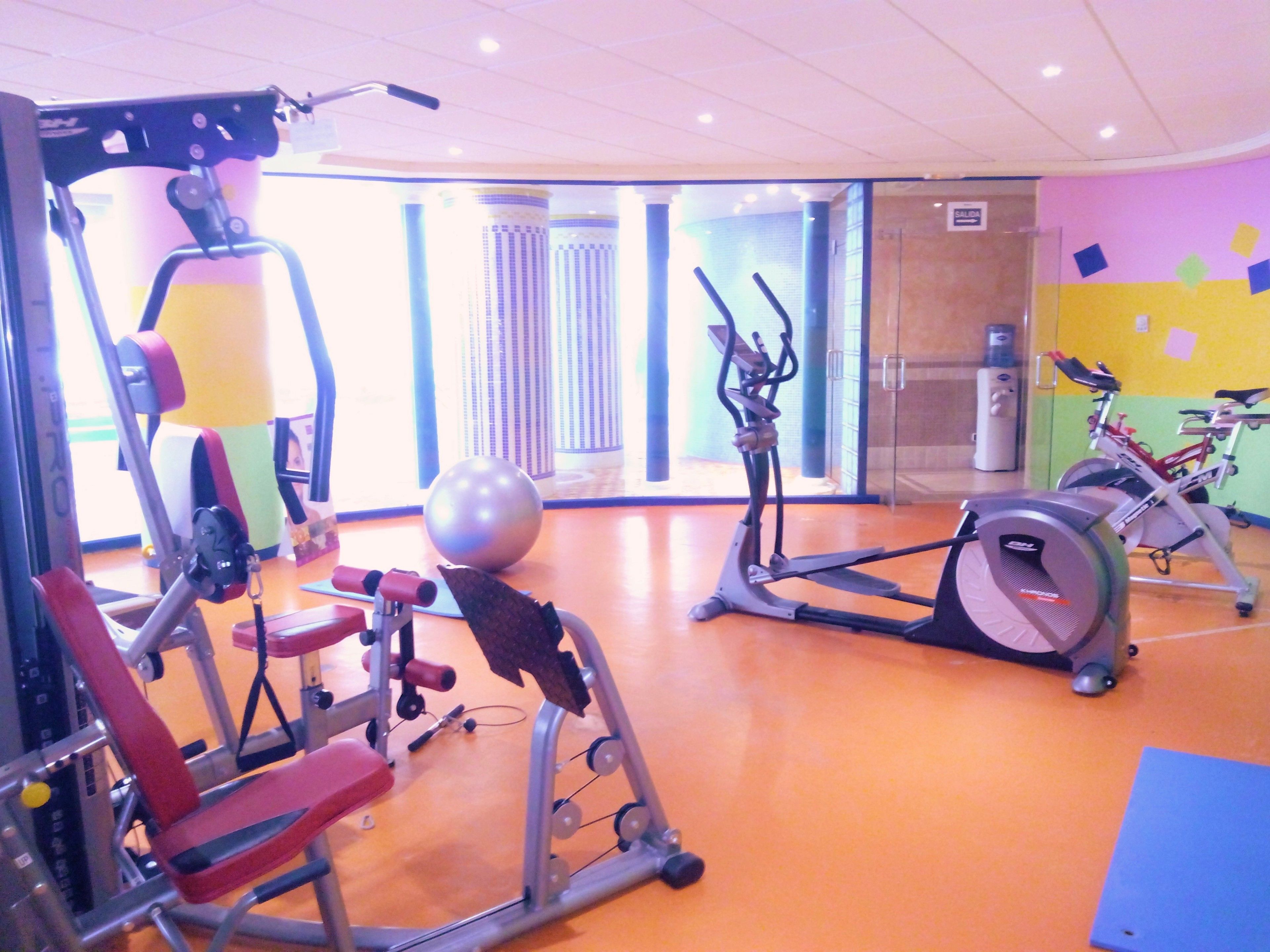 Un gimnasio con diversos equipos de ejercicio, incluyendo una máquina de remo, una elíptica y máquinas de pesas.