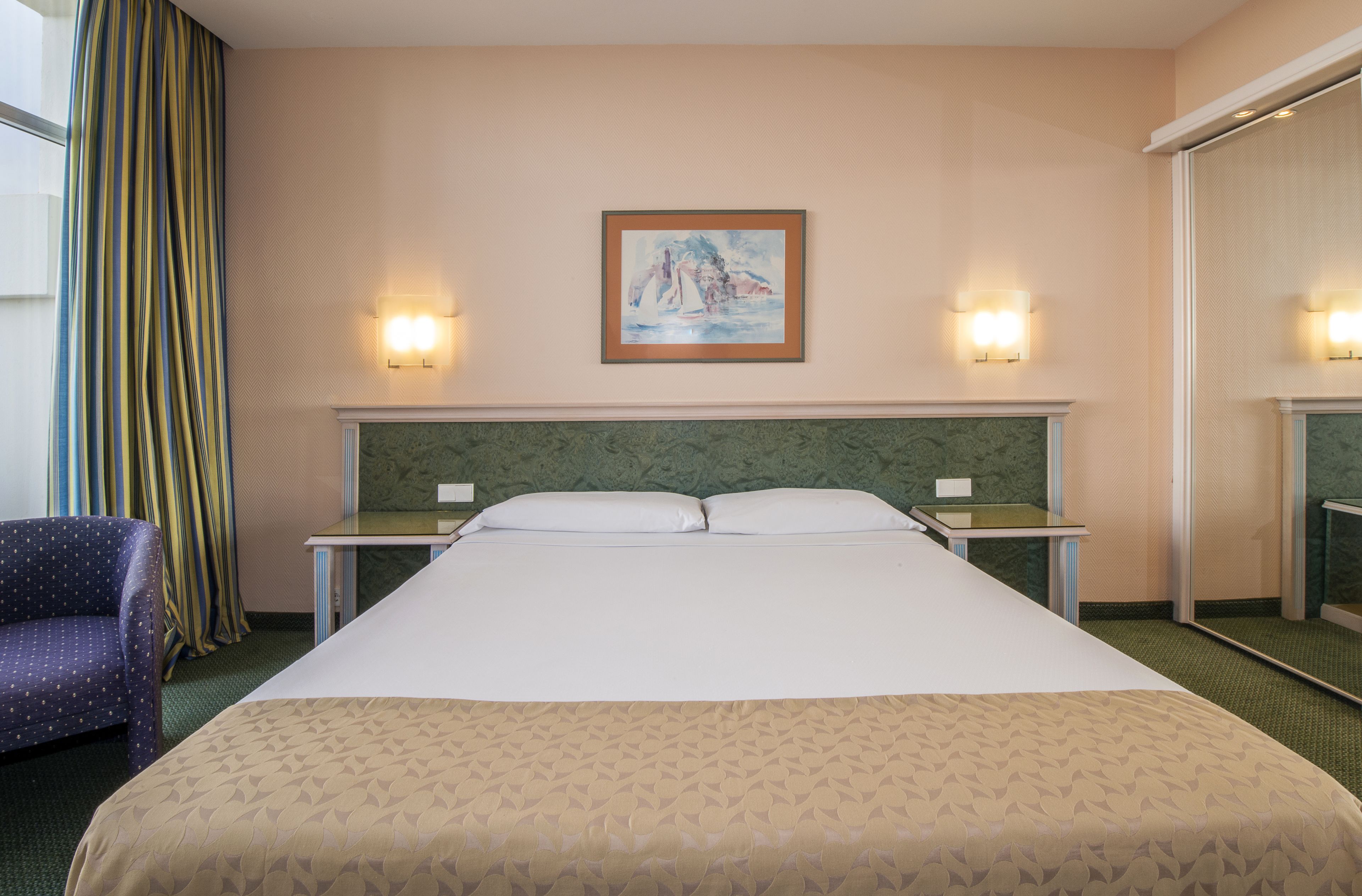 A hotel room with a large bed, two bedside tables, a chair, and a painting on the wall.