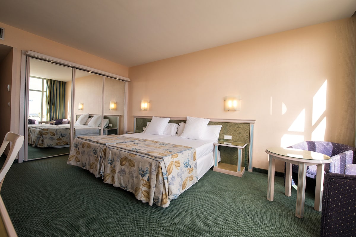 A hotel room with a bed, a chair, a small table, and a mirror.