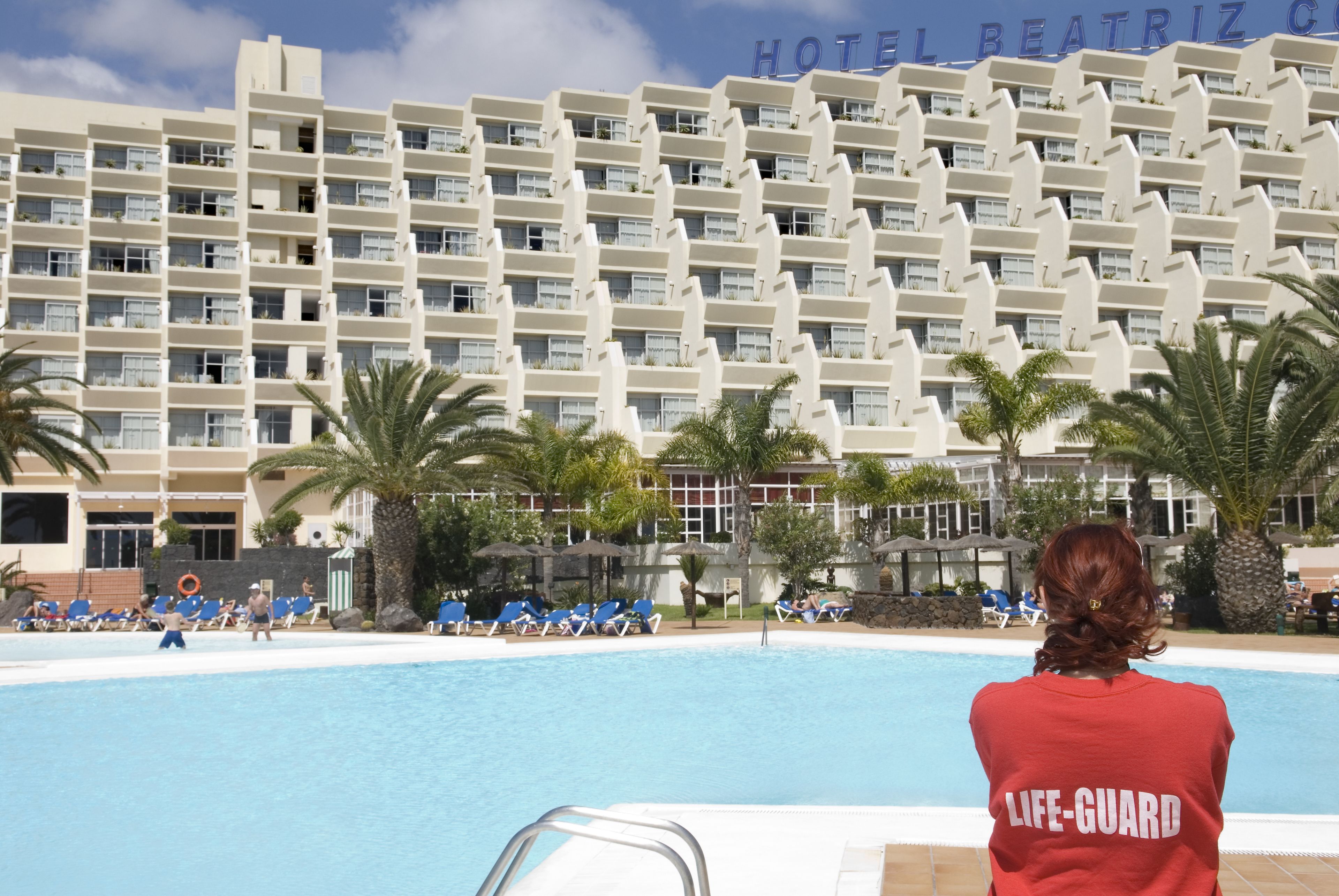 Un hotel con zona de piscina, socorrista de guardia y un cartel que dice "HOTEL BEATRIZ".