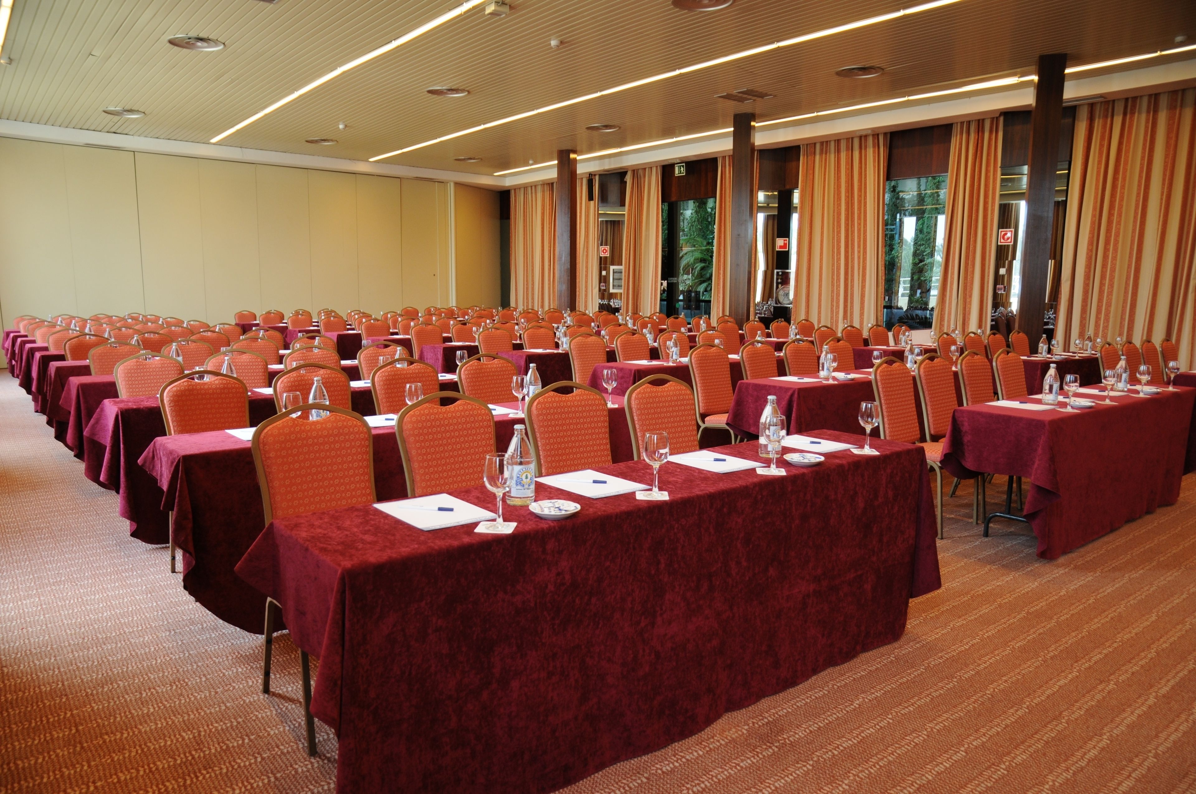 A conference room with rows of tables and chairs, equipped with water bottles and wine glasses.