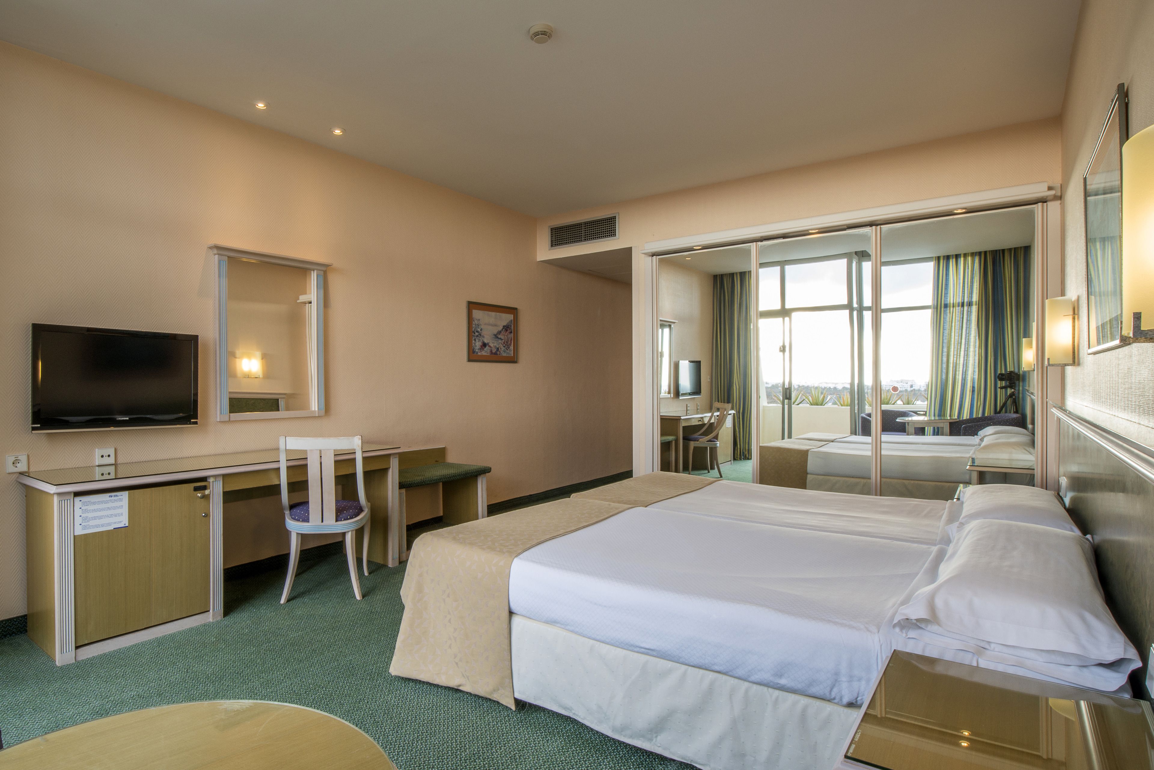 Une chambre d’hôtel équipée d’un lit, d’un bureau, d’une chaise, d’une télévision et d’une grande fenêtre.