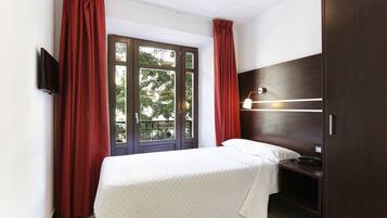 A bedroom with a bed, a bedside table, a TV mounted on the wall, and a window with curtains.