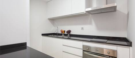Una cocina moderna con gabinetes blancos, encimera negra, electrodomésticos de acero inoxidable y horno integrado.