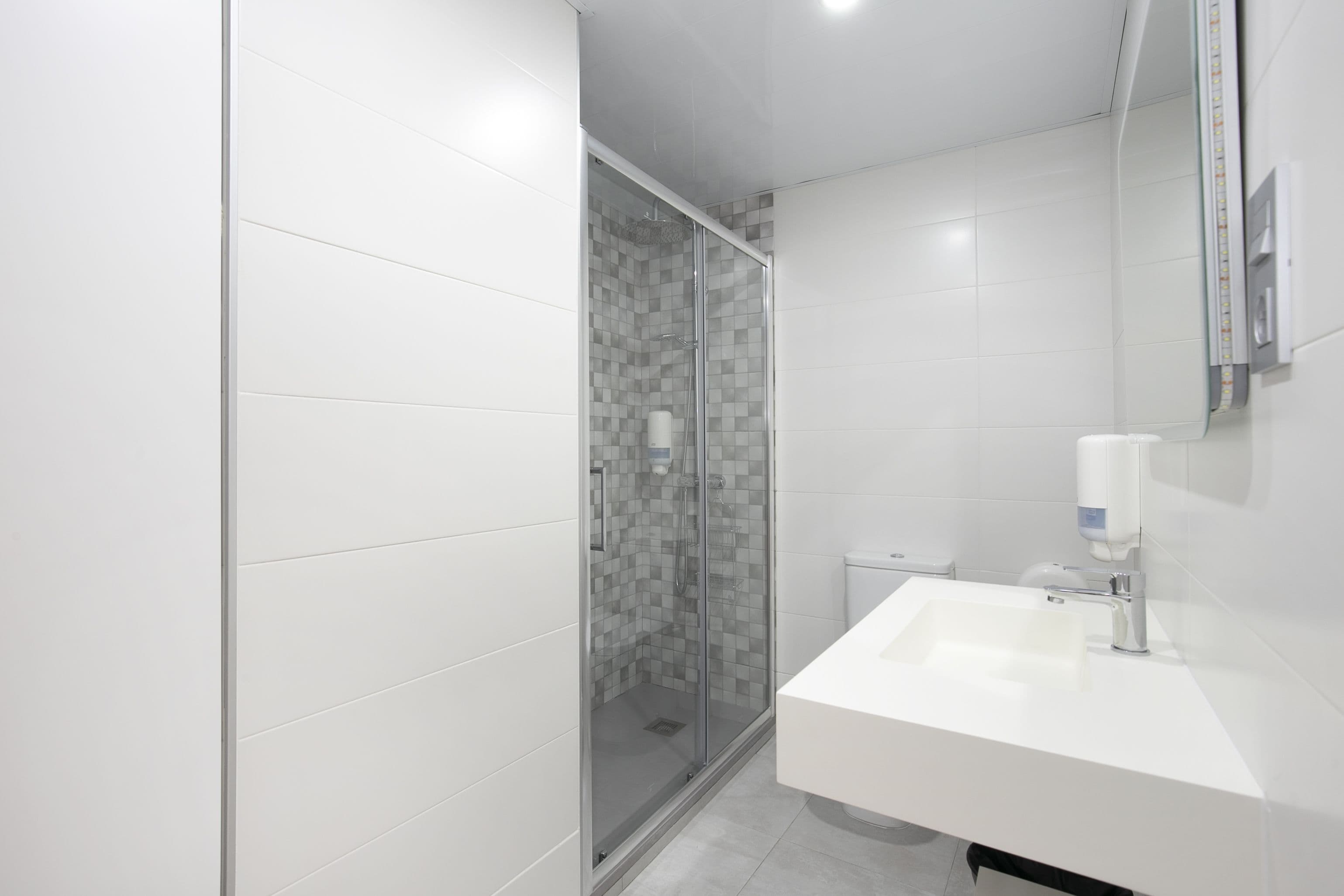 Un baño moderno con ducha de vidrio, lavamanos blanco y espejo.