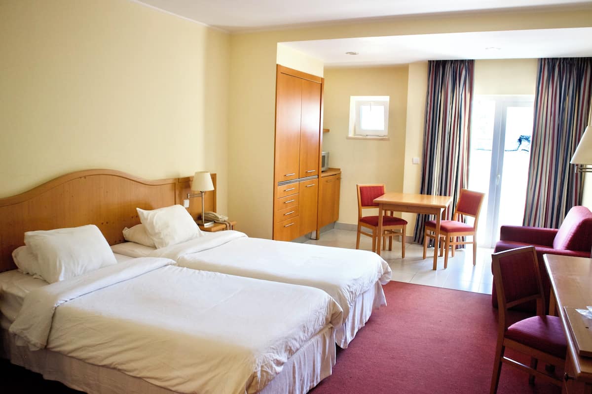 A hotel room with two beds, a desk, chairs, a wardrobe, and a window with curtains.