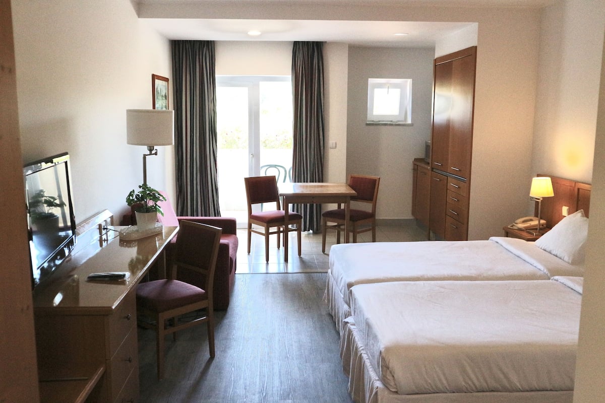 A hotel room with two beds, a desk with a chair, a TV, and a window with curtains.