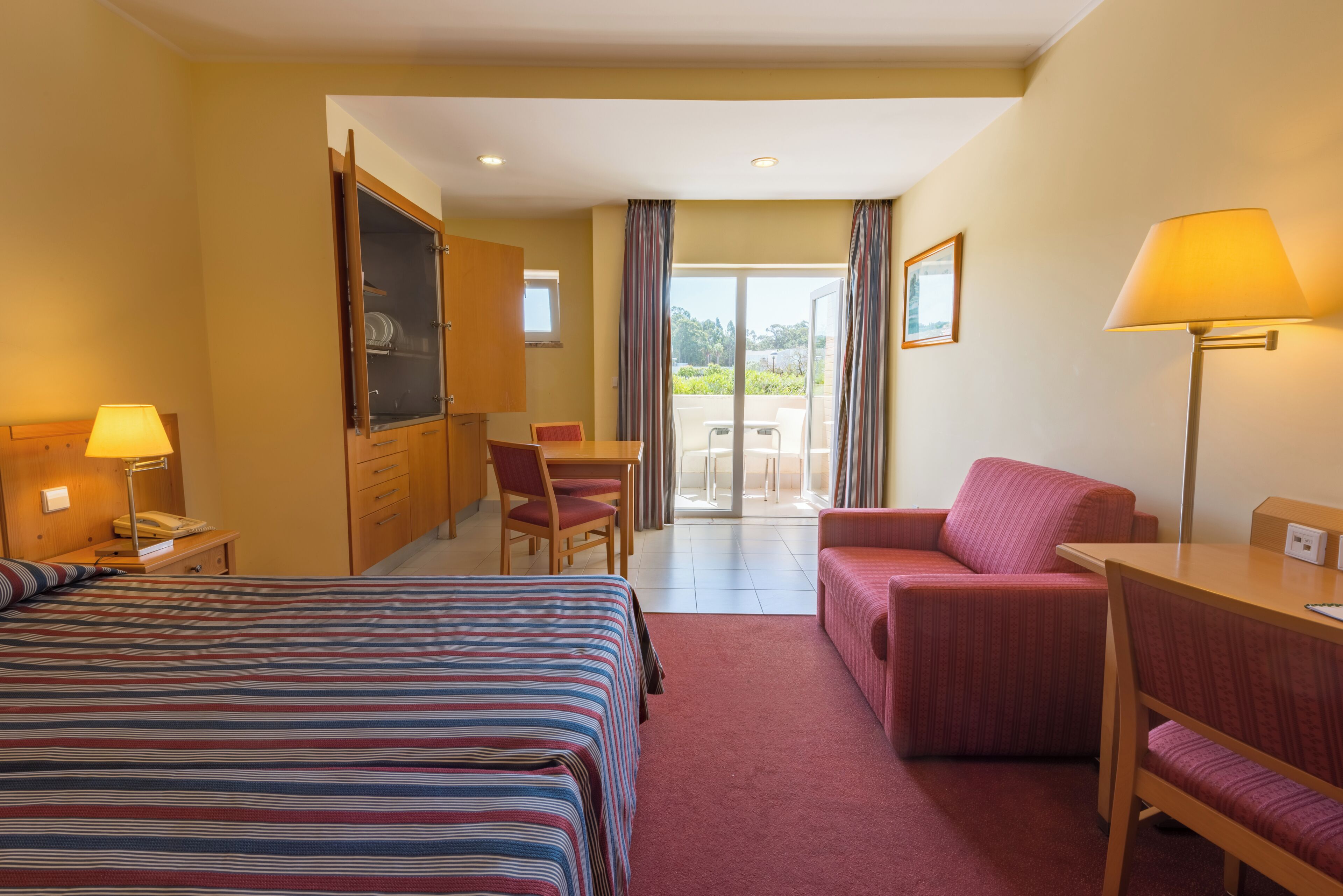 Ein Hotelzimmer mit Bett, Schreibtisch, Sessel und einer Aussicht ins Freie.
