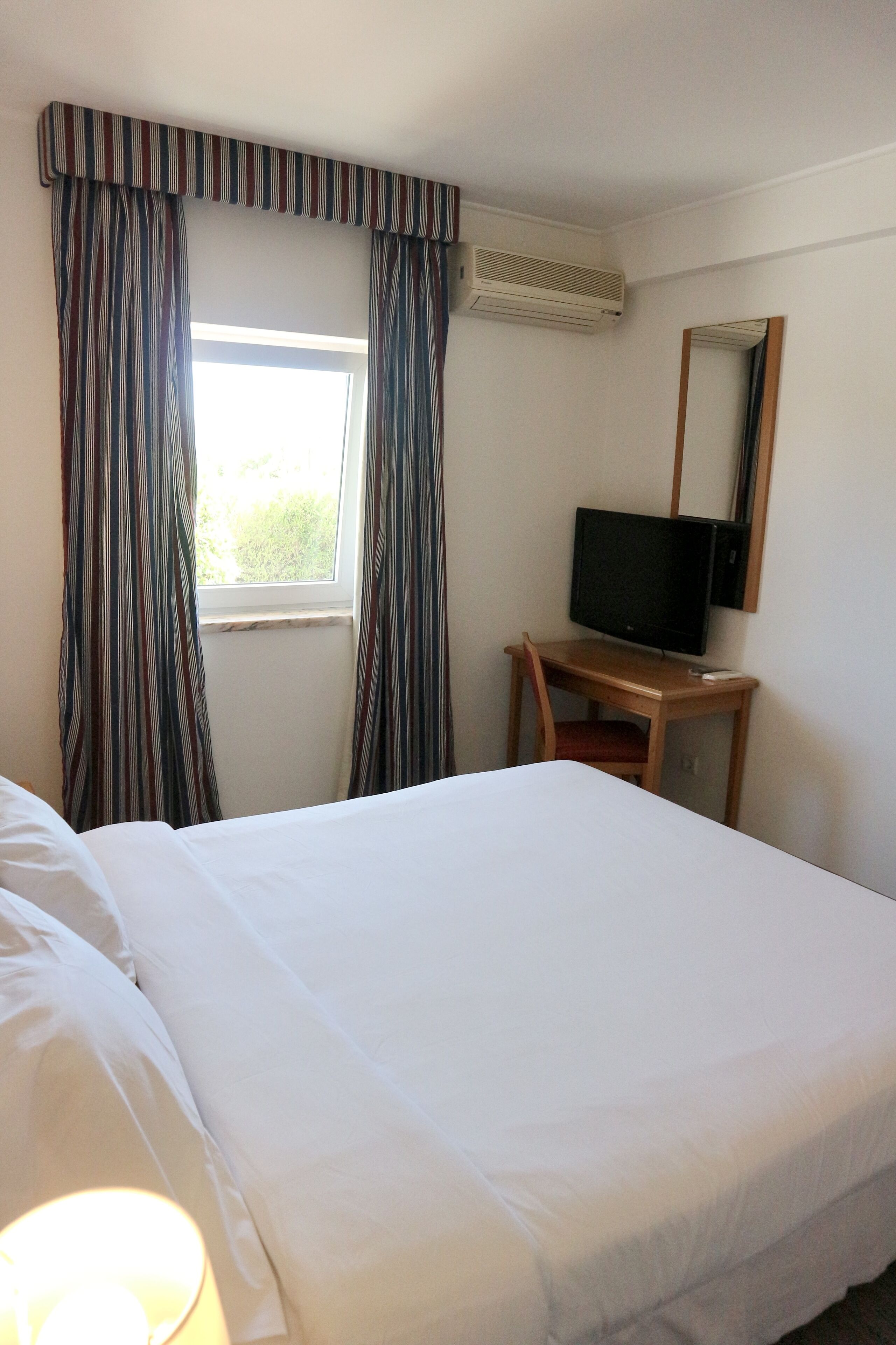 Ein Hotelzimmer mit einem Bett, einem Schreibtisch mit Fernseher und Vorhängen.