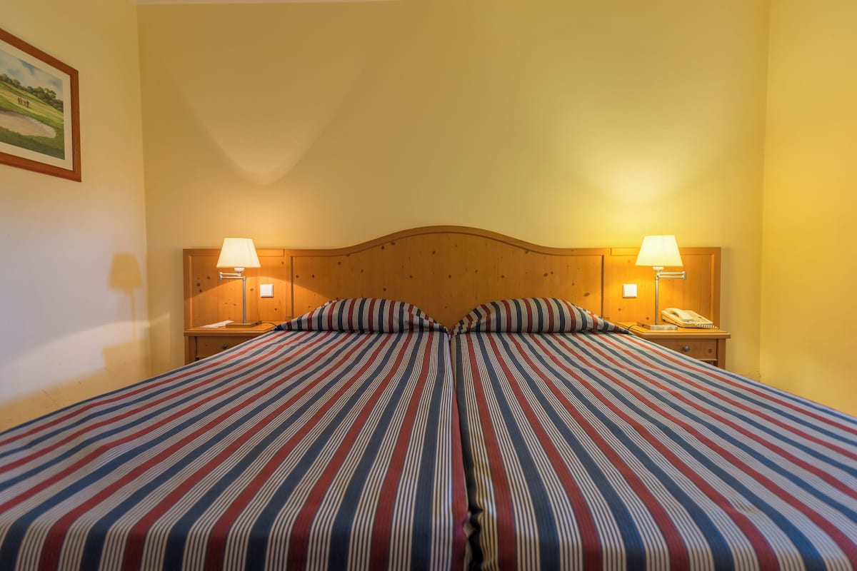 A double bed with striped bedding, two bedside lamps, a wooden headboard, and a framed picture on the wall.