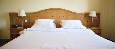 A neatly made bed with white linens and pillows, two bedside lamps, and a folded towel on the bed.