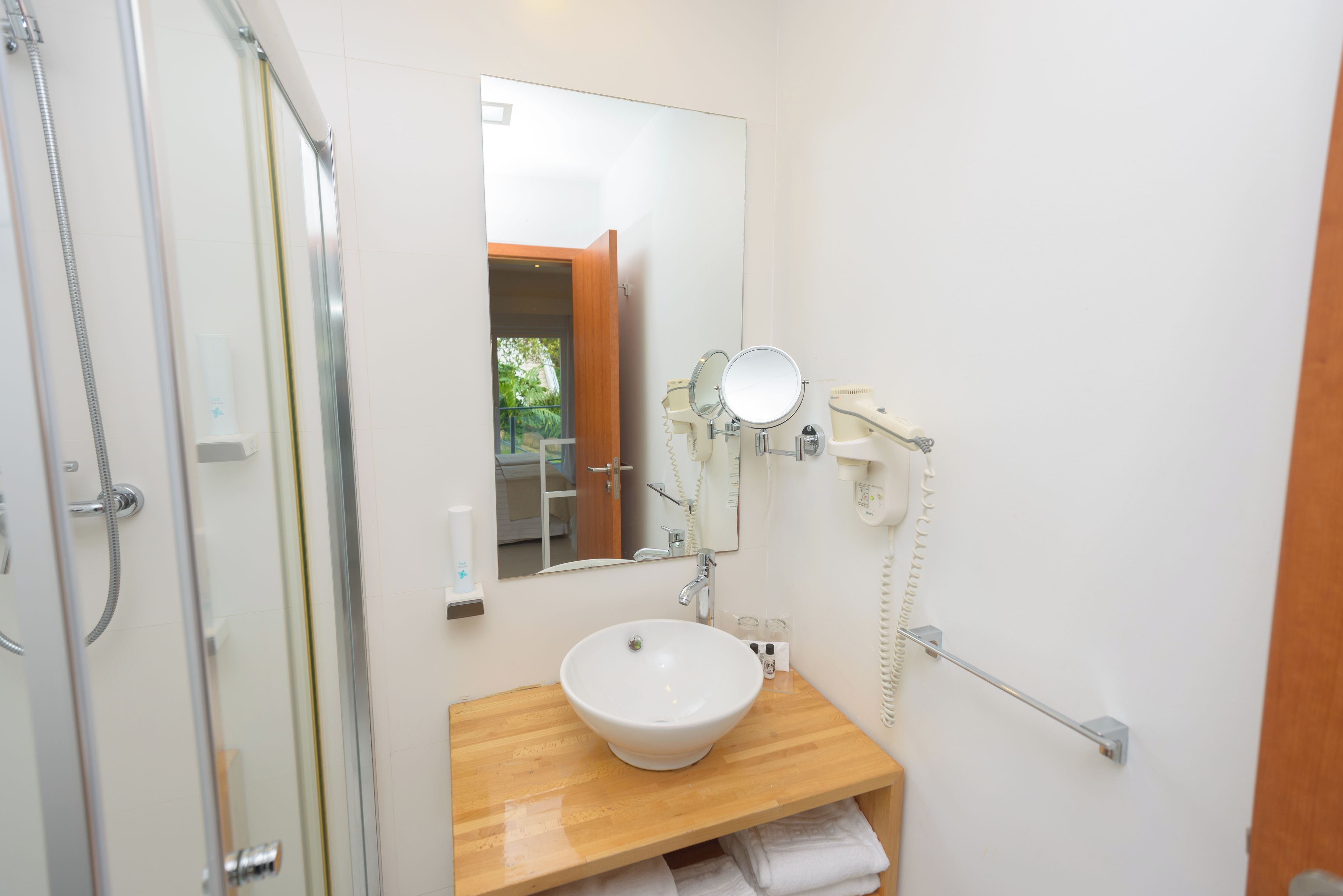 A bathroom with a wooden vanity, a white sink, a mirror, a handheld showerhead, and a towel rack.