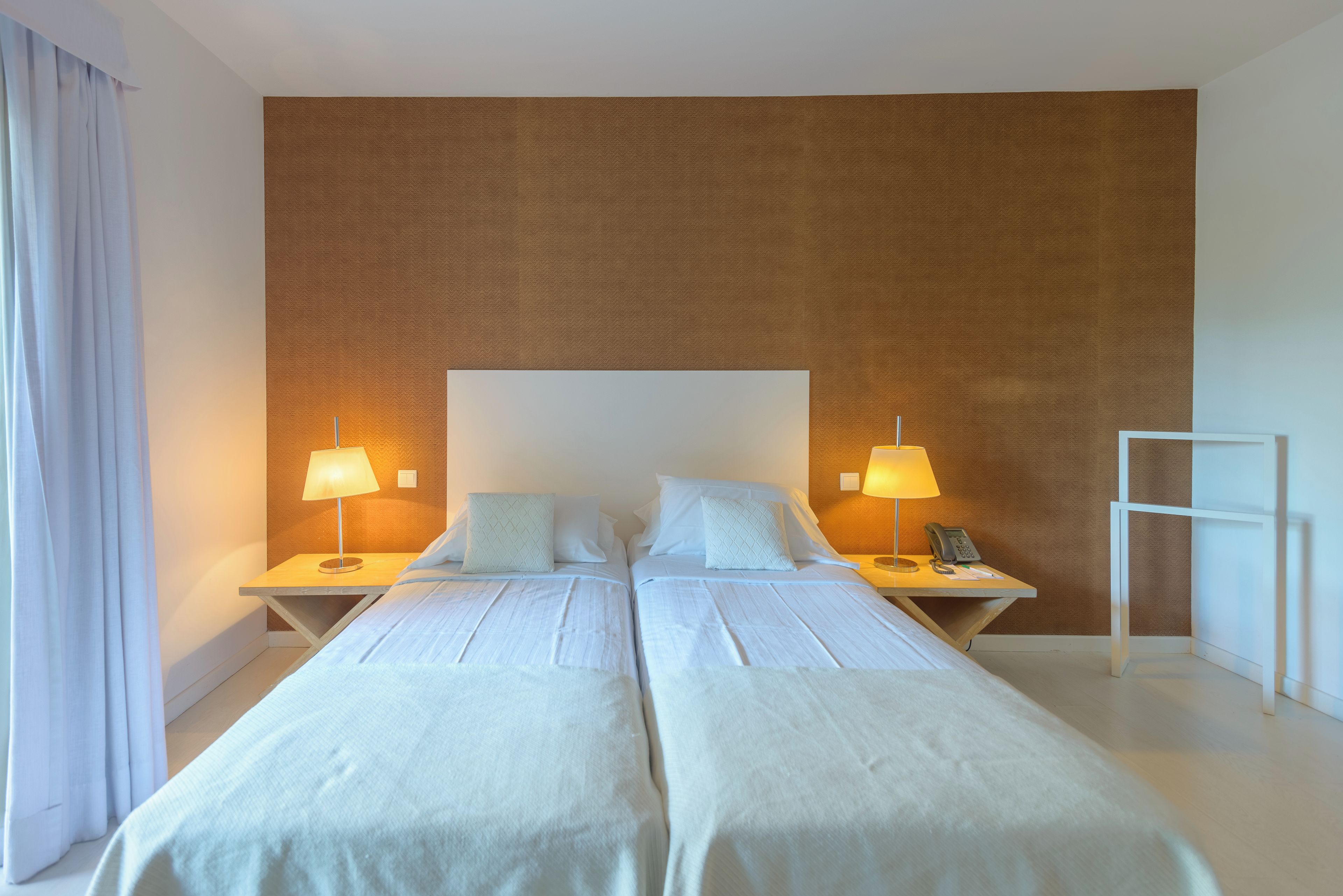 A hotel room with two beds, a large window with curtains, and a wall with a textured pattern.