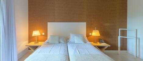 A hotel room with two beds, a large window with curtains, and a wall with a textured pattern.