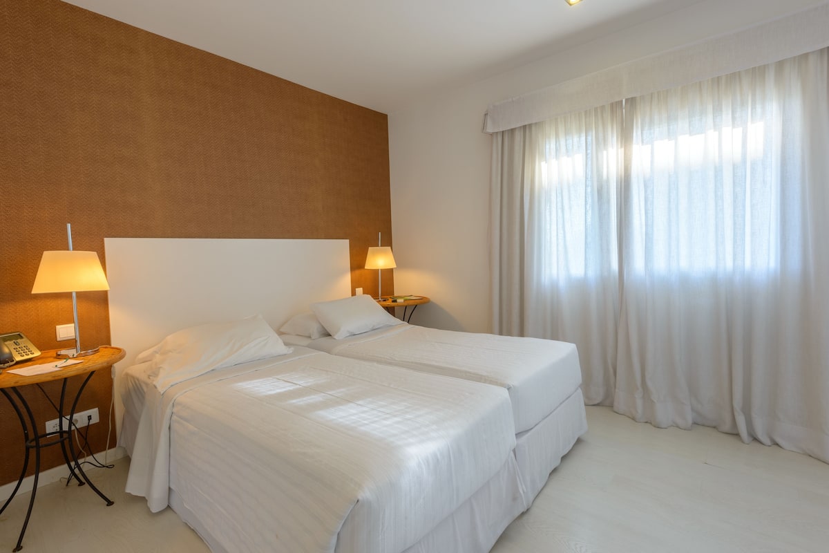 A hotel room with two beds, a desk with a lamp, and a telephone.