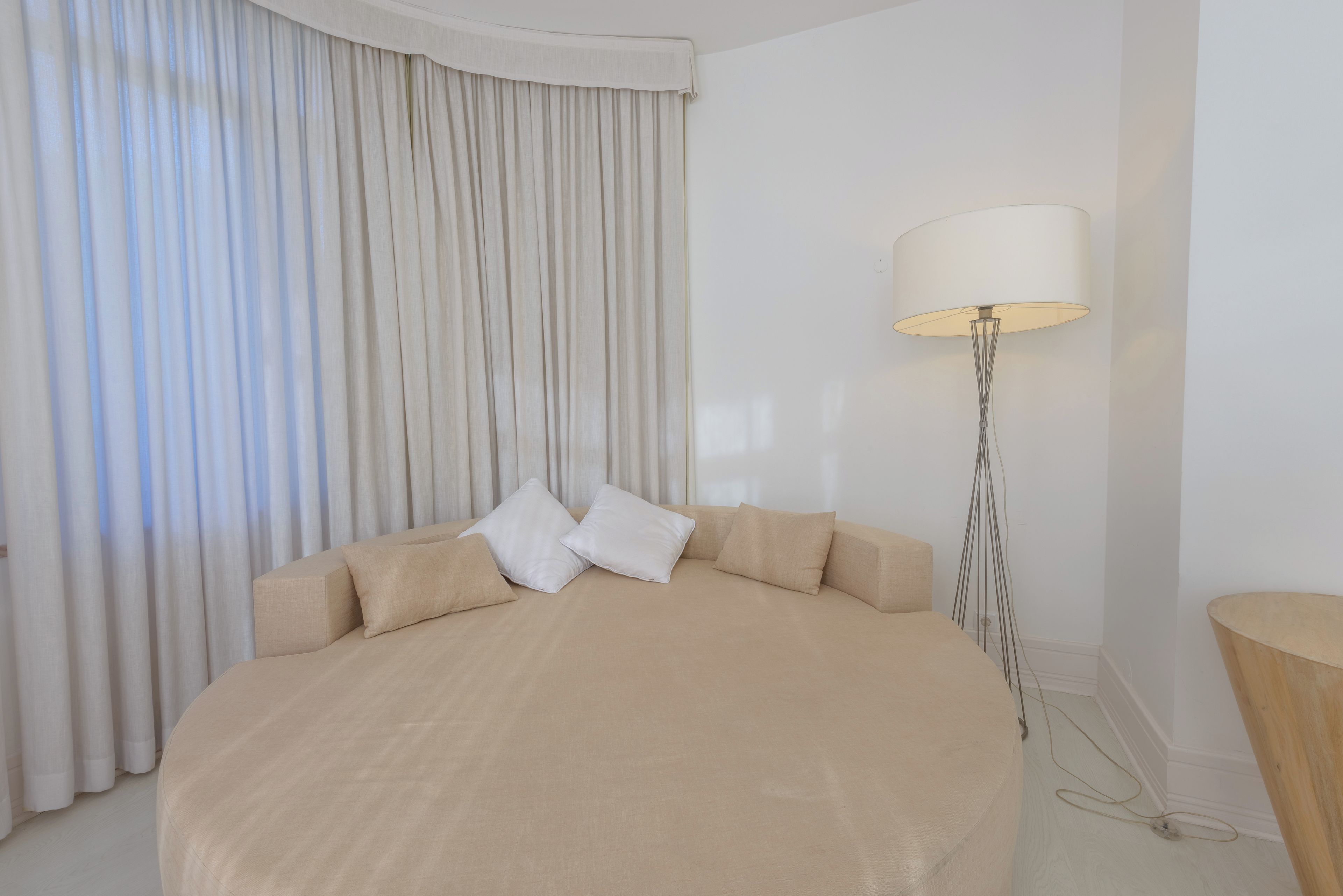 A bedroom with a large bed, a floor lamp, and a view of the outdoors through curtains.