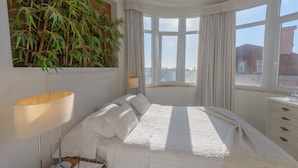 Un dormitorio con una cama grande, una mesita de noche, una lámpara y un ventanal con cortinas.