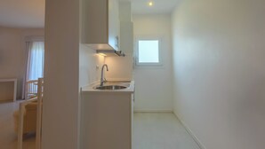 Una cocina estrecha con paredes blancas, un lavamanos integrado y una ventana.