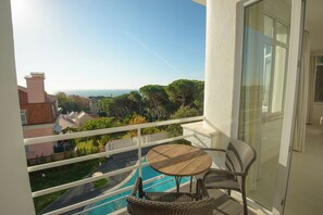 A balcony with a view of the sea, a pool, and surrounding greenery. - Amazonia Estoril Hotel (Cascais)