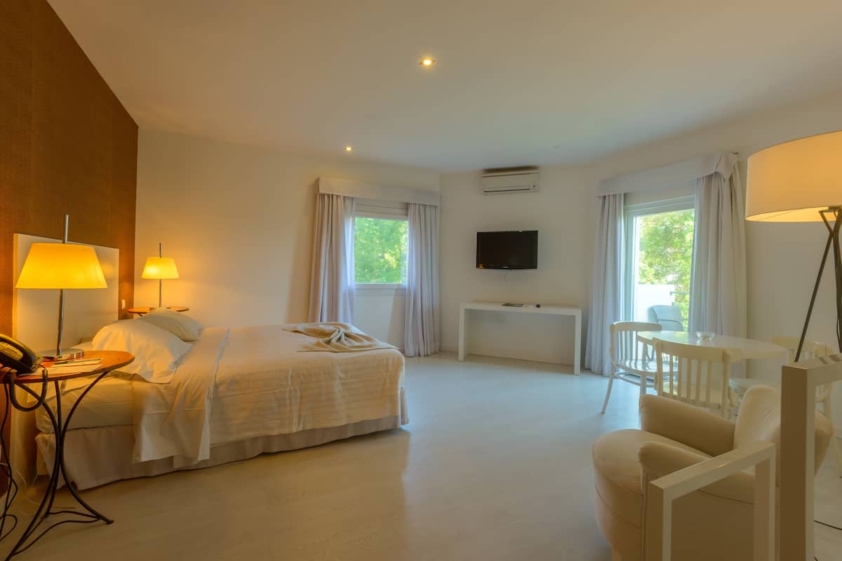 A hotel room with a bed, bedside table, lamp, TV, and a seating area with a chair and table.