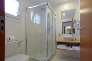 Un baño moderno con ducha de vidrio, lavabo blanco y espejo sobre el lavabo.