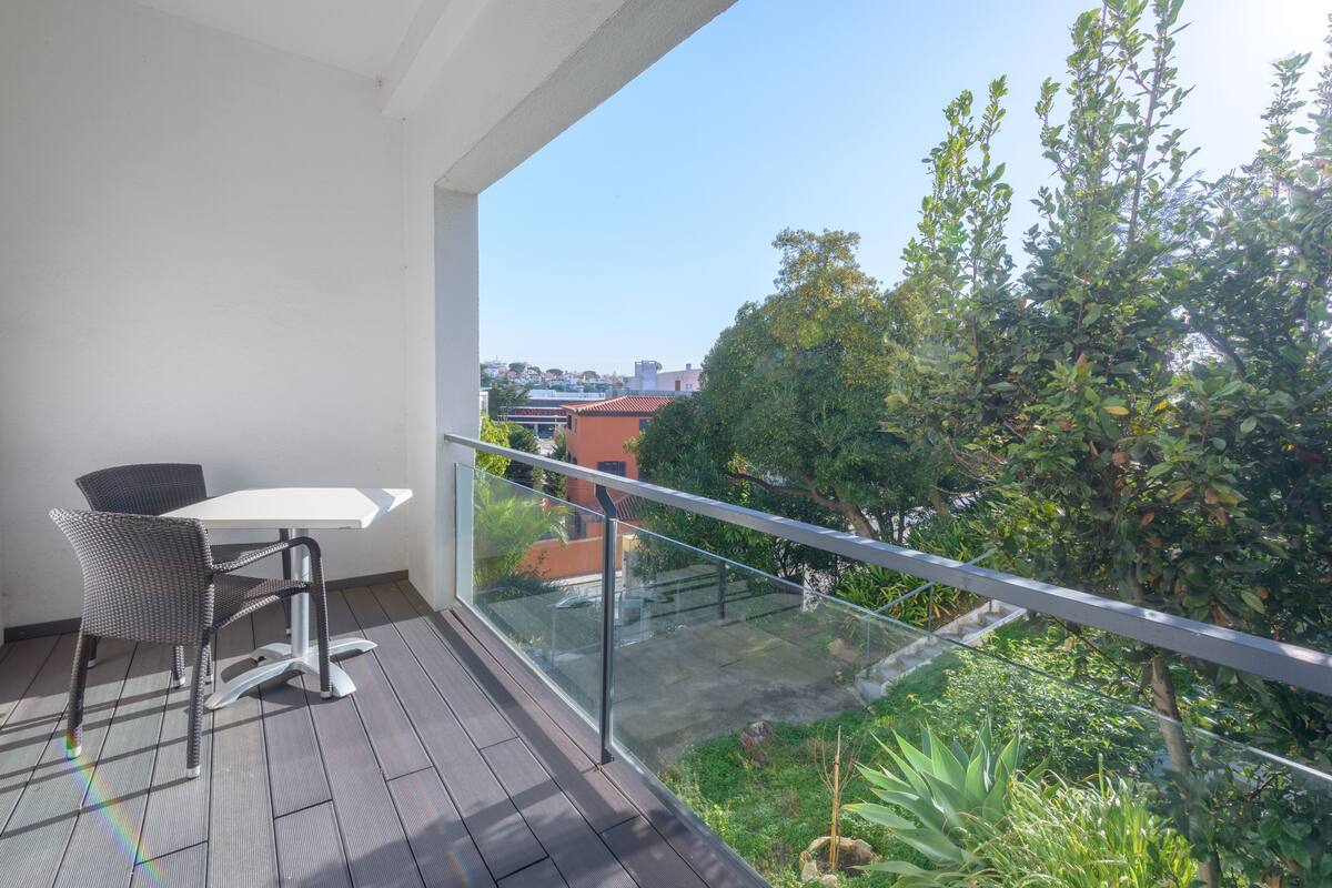 A balcony with a glass railing, a table, and two chairs.