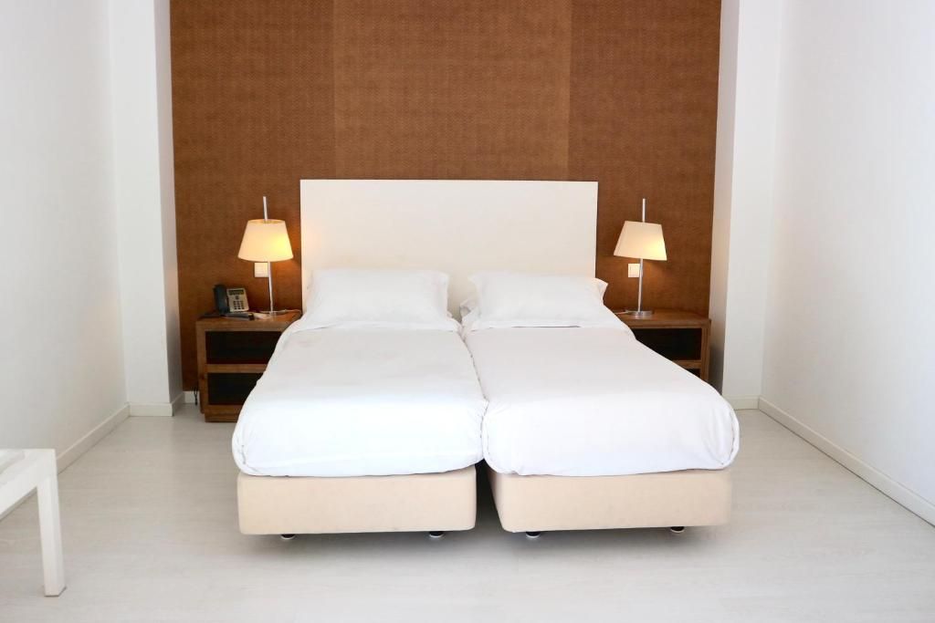 A double bed with white bedding, two bedside tables with lamps, and a wooden headboard.