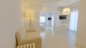 Una habitación de hotel moderna y minimalista con sofá, una mesita, televisión y un comedor con sillas.
