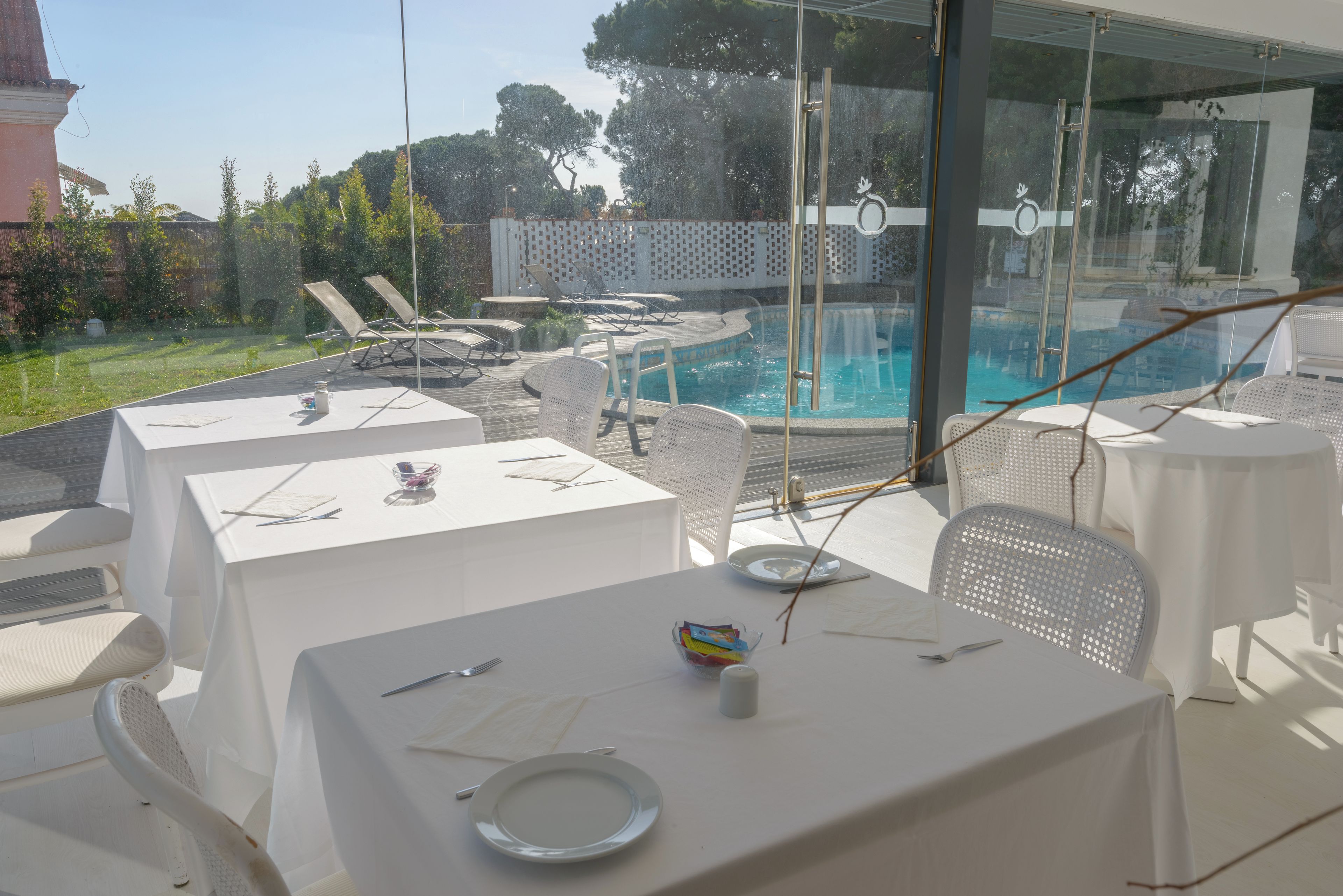 Un área de comedor al aire libre con mesas, sillas y una piscina al fondo.