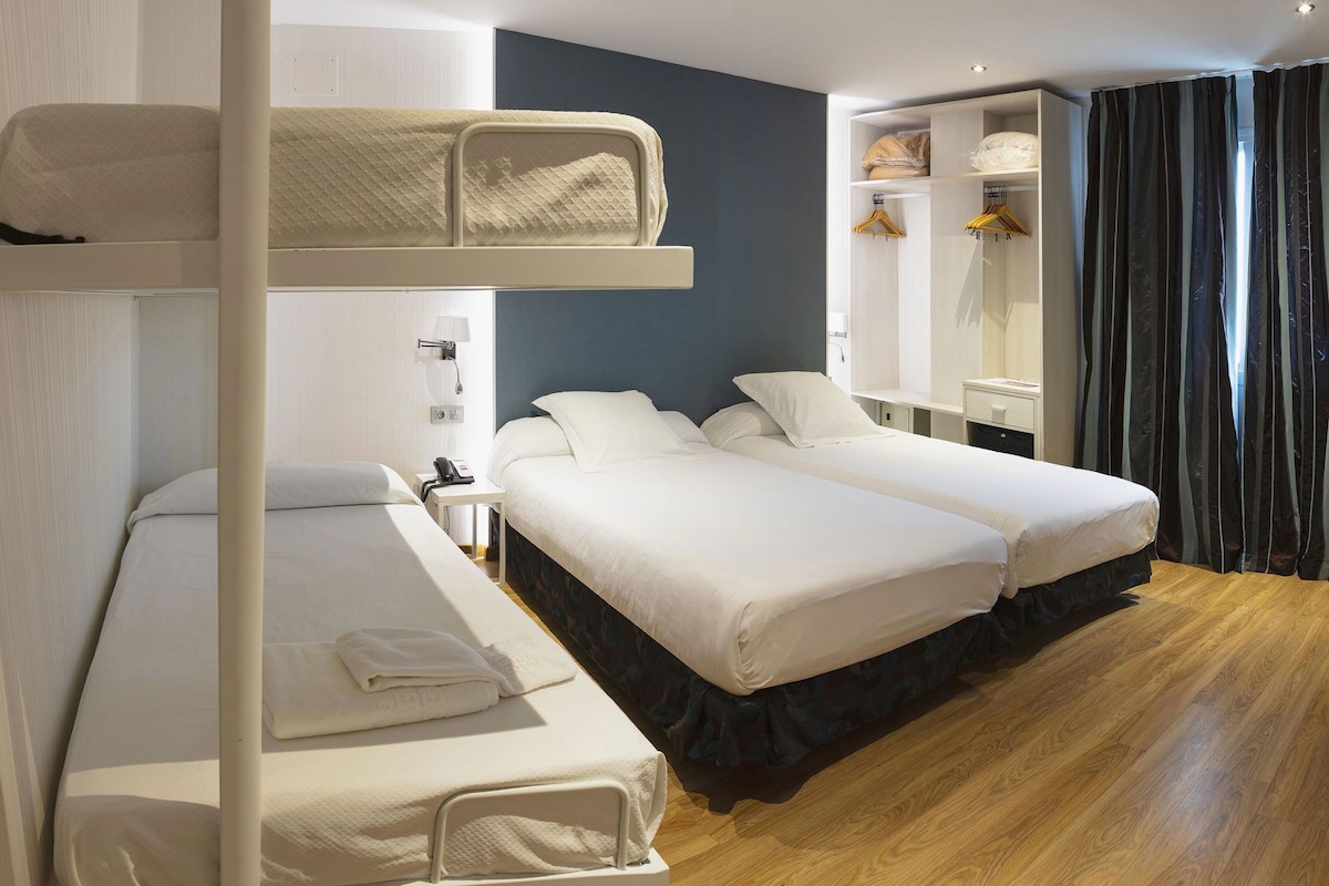 A hotel room with bunk beds, a desk, a wardrobe, and a bathroom.