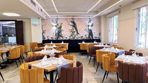 Un restaurant doté de nombreuses tables et chaises, d’une fresque représentant des oiseaux et de grandes fenêtres.