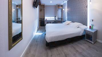 Habitación de hotel con cama, mesita de noche, espejo, armario, escritorio y una pequeña kitchenette.