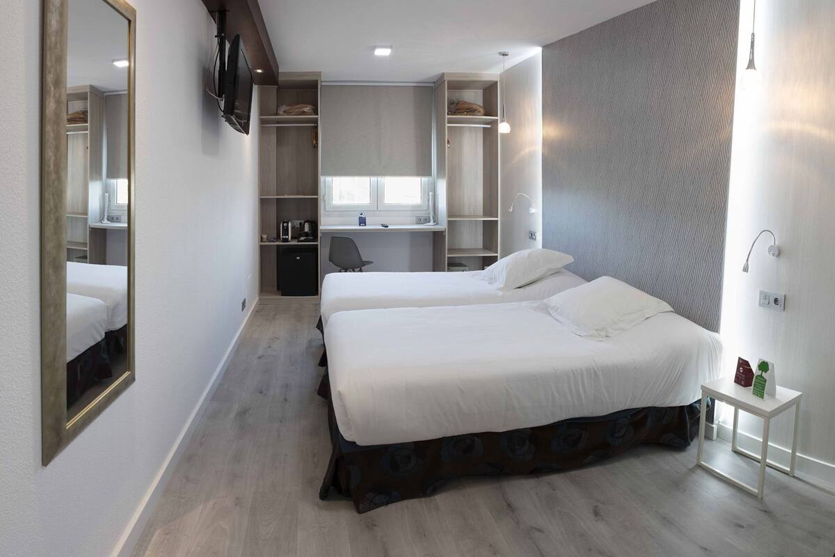 A hotel room with two beds, a desk, a wardrobe, and a TV.