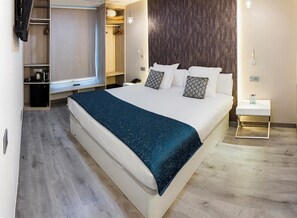 Ein modernes Hotelzimmer mit einem großen Bett, einem Nachttisch, einem Kleiderschrank, einem Schreibtisch und einem kleinen Badebereich.