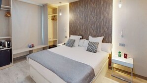 Une chambre d’hôtel moderne avec un grand lit, des tables de chevet, une armoire et un miroir.