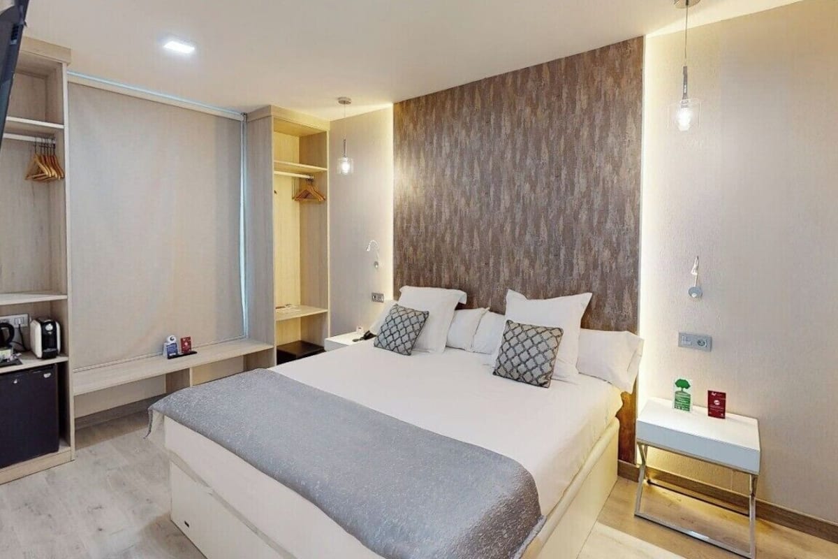 A modern hotel room with a large bed, bedside tables, a wardrobe, and a mirror.