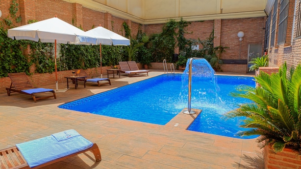 Une piscine entourée de murs en briques et de verdure, avec des chaises longues et des parasols.