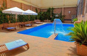 A swimming pool with lounge chairs and umbrellas, surrounded by brick walls and greenery. - Hotel Bellavista Sevilla (Seville)