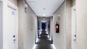 Un couloir d’hôtel avec un tapis à rayures, des portes blanches et un extincteur fixé au mur.