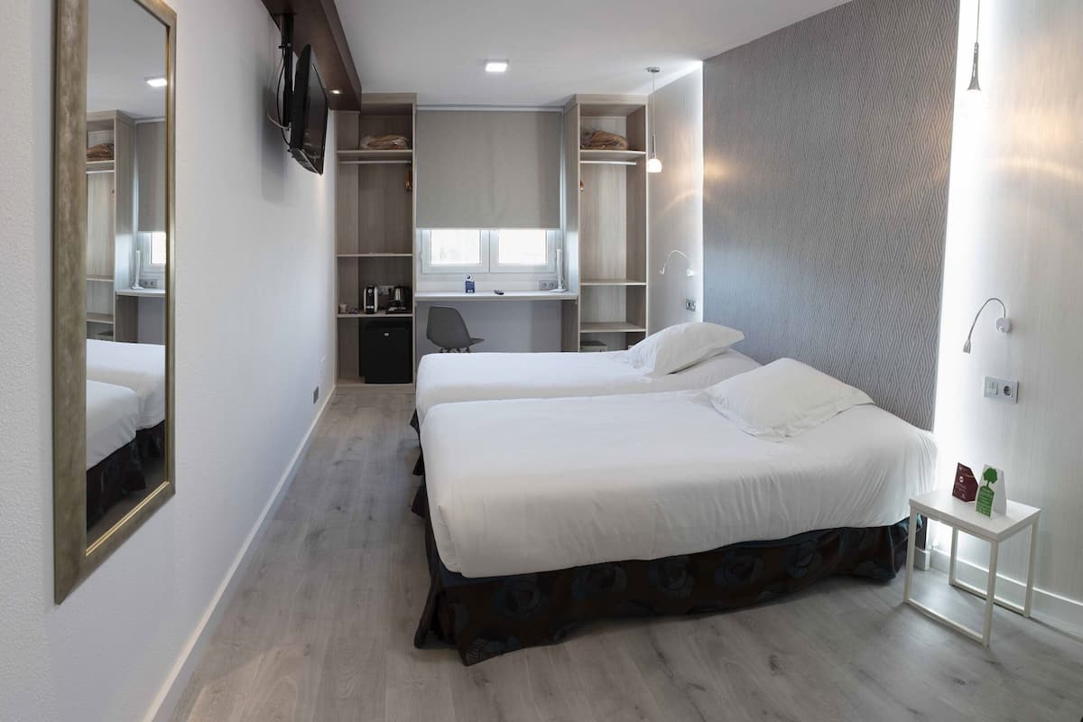 A hotel room with two beds, a desk, a wardrobe, and a TV.