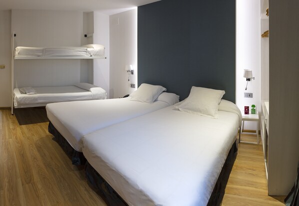 Habitación de hotel con dos camas, piso de madera, pared de acento oscura y una mesita de noche con lámpara.