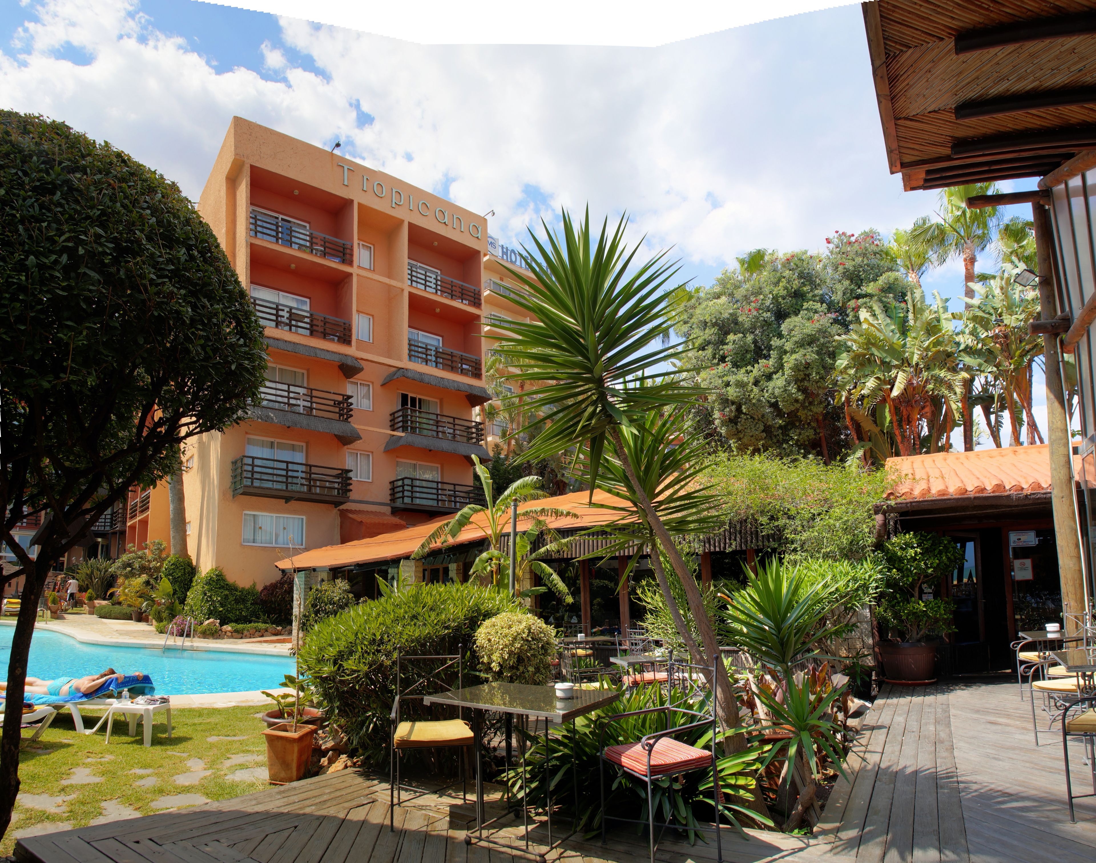 A hotel with a pool, outdoor seating, and lush greenery.