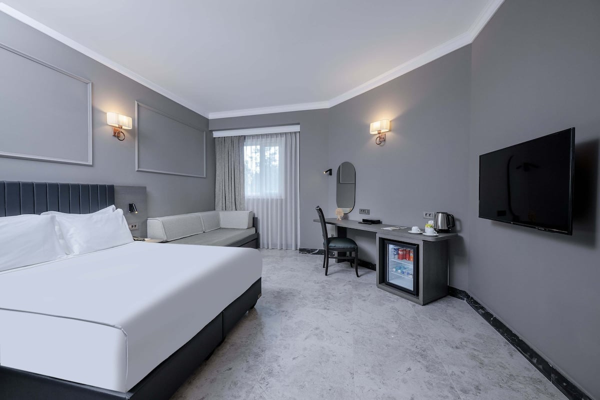 Ein Hotelzimmer mit Bett, Schreibtisch, Stuhl, Fernseher und Minibar.