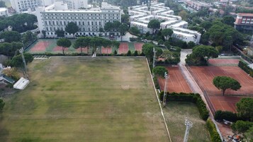 An aerial view of a residential area with multiple tennis courts, a large building with balconies, and surrounding greenery.
