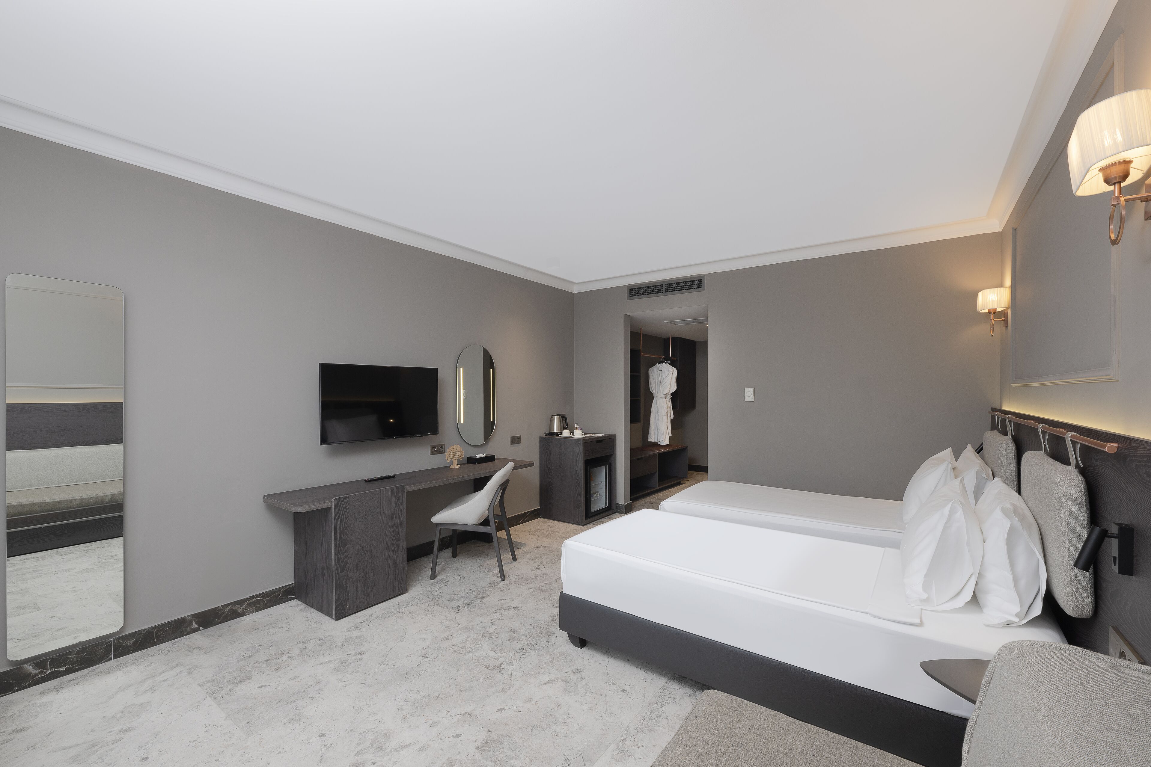A modern hotel room with a large bed, a desk, a chair, a TV, and a mirror.